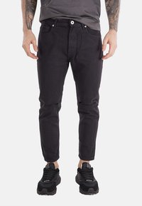 Jeans neri a gamba tapered con vestibilità slim, caratterizzati da chiusura frontale con bottone, cinque tasche e dettagli strappati sulle ginocchia.