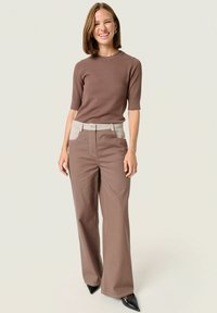 Brown ribbed knit top with short sleeves paired with high-waisted brown wide-leg pants, featuring beige accents on the waistband. Black pointed shoes.