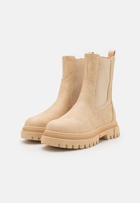 Bottines beiges en daim avec des panneaux élastiques sur les côtés, une semelle plateforme légèrement surélevée et un profil texturé pour une meilleure adhérence.