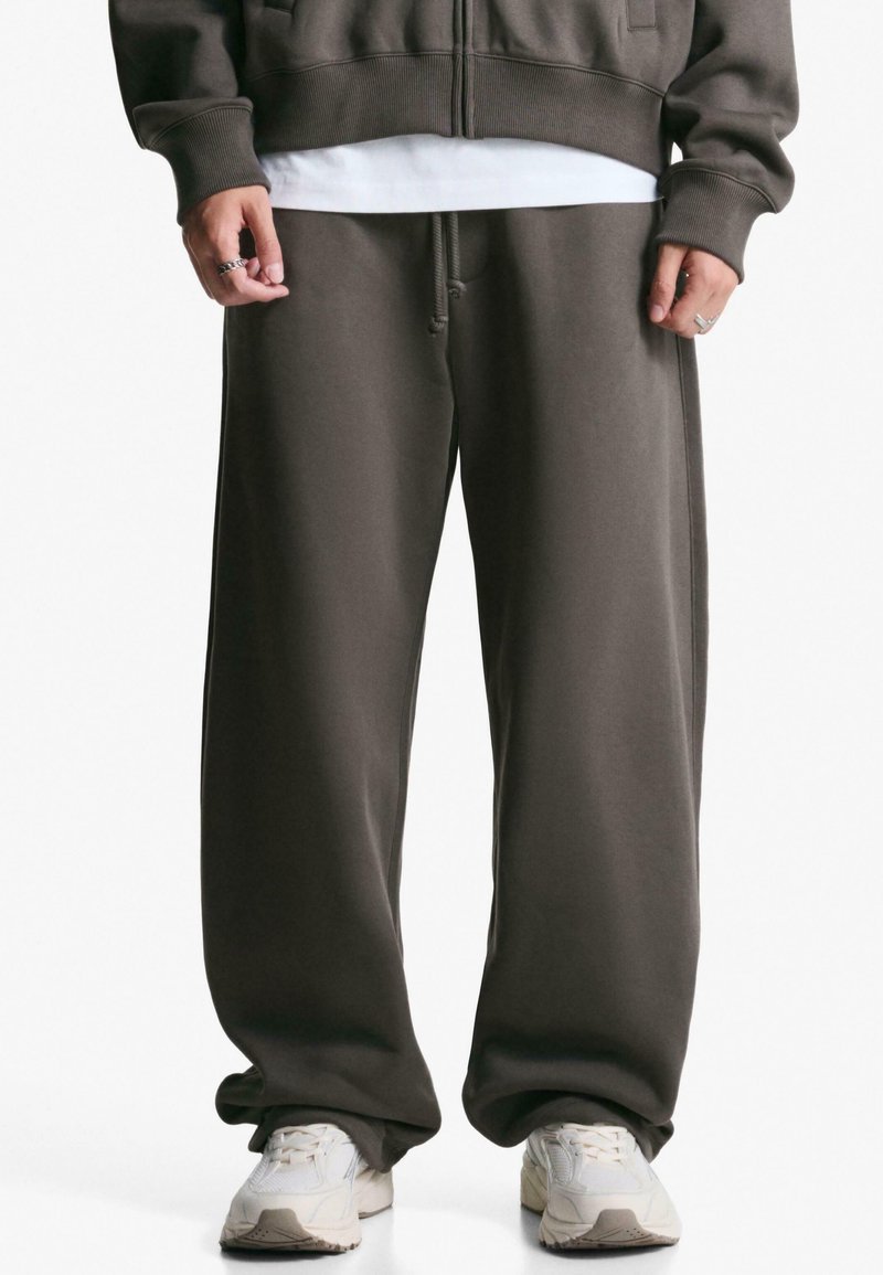 Ciemnobrązowe spodnie dresowe o luźnym kroju, wykonane z miękkiego materiału, z elastycznym pasem i bocznymi kieszeniami. Połączone z białymi trampkami.