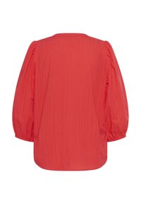 Röd, ribbade blus med rund halsringning och långa, puffiga ärmar. Materialet verkar lätt och något texturerat. Nederkanten är krökt.