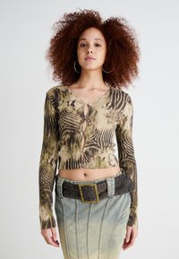 Haut court à manches longues en olive et beige avec imprimé animal, doté de boutons en trou de serrure à l'avant. Associé à une jupe en denim et une ceinture.