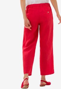 Femme portant un pantalon rouge ample avec une taille élastique et des chaussures plates rouges à bride arrière, vue de dos.