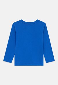 Ilgos rankovės marškinėliai iš vientisos ryškiai mėlynos medvilnės. Apvalus kaklas, laisvas kirpimas, su apvirstais rankogaliais ir tiesiu apačios kraštu, be matomų logotipų ar dizainų.