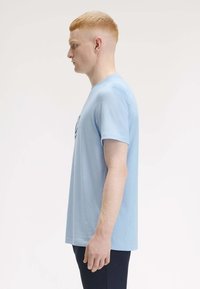 Helles blaues Baumwoll-T-Shirt mit kurzen Ärmeln, rundem Halsausschnitt, mit einem grafischen Druck auf der Vorderseite, seitlich betrachtet.