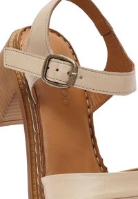 Sandalo con tacco alto in pelle beige, dotato di una fascia larga, fibbia regolabile alla caviglia e tacco a blocco in legno strutturato. Fodera interna morbida.