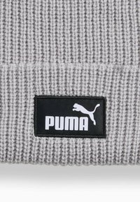 Grå strikket beanie med ribbestruktur, prydet med et sort rektangulært patch med den hvide "PUMA"-logo og en springende puma-silhuet.