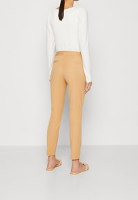 Beige op maat gemaakte broek met een gladde textuur, achterzakken, gecombineerd met een witte blouse met lange mouwen die een gestructureerde achterkant en een aansluitend ontwerp heeft.