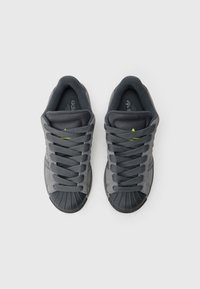 Γκρι αθλητικά παπούτσια με υφή υφάσματος στο πάνω μέρος, μαύρο ελαστικό κάλυμμα στα δάχτυλα και χοντρές γκρι κορδόνια. Διαθέτουν πράσινο λογότυπο στη γλώσσα.