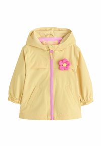 Chaqueta impermeable amarilla con capucha, cremallera rosa, bolsillos frontales y un adorno rosa desmontable en forma de flor en el pecho. Textura suave.