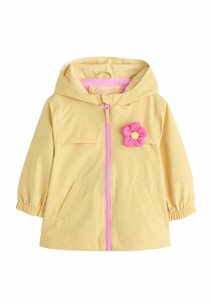 Chaqueta impermeable amarilla con capucha, cremallera rosa, bolsillos frontales y un adorno rosa desmontable en forma de flor en el pecho. Textura suave.