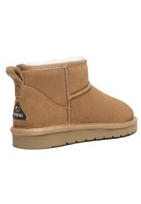 Beige Wildleder-Ankle-Boot mit weichem Innenfutter, abgerundetem Zehenbereich und flacher Gummisohle. Mit einem Logo-Patch und einer Schlaufe zum einfachen Anziehen.