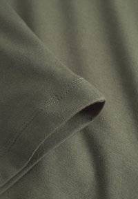 Gros plan sur un tissu vert olive montrant un ourlet à double couture sur le bord plié d'une manche de vêtement.
