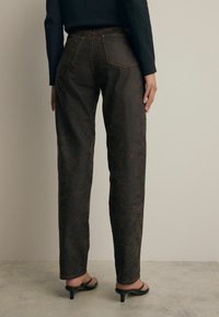 Pantalones de mezclilla marrones con patrón y corte recto, que cuentan con dos bolsillos traseros y detalles de costura sutiles.