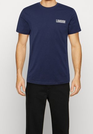 Man wearing a navy blue short-sleeve t-shirt with "LONDON" text on the left chest, paired with black pants.