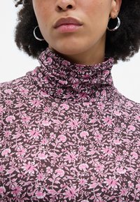 Suéter de cuello alto marrón con un patrón de flores en tonos rosa y blanco, fabricado en una tela suave con un acabado texturizado y un diseño ajustado.