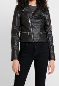 Svart lädermotorcykeljacka med figursydd design, asymmetrisk dragkedja, silverdetaljer och två framfickor med dragkedja. Lätt textur.