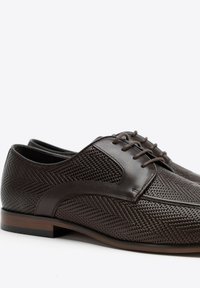 Scarpe da cerimonia in pelle marrone con un design a pannelli in rete testurizzati. Presentano una punta arrotondata, lacci e una suola piatta in gomma scura.