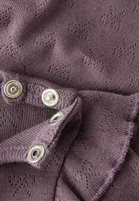 Stickad lila tyg med en texturerad mönster, med rundade silverknappar längs kanten och en volangdetalj.