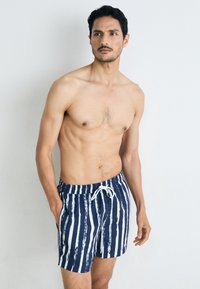 Marineblaue Badehose mit weißen vertikalen Streifen, elastischem Bund mit Kordelzug, seitlichen Taschen, aus leichtem Material.