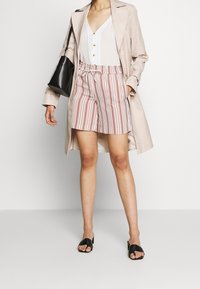 Pruhované šortky v bílé a červené barvě s elastickým pasem, doplněné lehkým béžovým trenčkotem a černými sandály. Jednoduchý top na knoflíky.