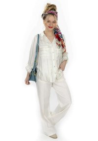 Chemise blanche à manches longues avec des rayures bleu clair, assortie à un pantalon large blanc. Une écharpe à motifs colorés et un sac à main teal complètent le look.