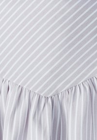 Svetlo levanduľová tkanina s bielymi vertikálnymi pruhmi, s volánovým lemom pozdĺž dolného okraja, predvádzajúca jemnú textúru.