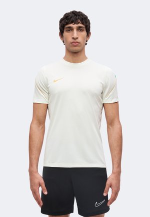 Homme debout de face, portant un t-shirt Nike blanc et un short Nike noir, bras détendus sur les côtés, expression neutre, fond uni.