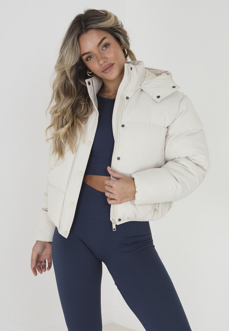 Doudoune beige clair avec un col montant, fermeture éclair et boutons-pression. Associée à des leggings côtelés bleu marine.