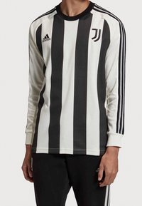 Sort og hvid langærmet trøje med lodrette striber, der har tre sorte striber på skuldrene, Adidas-logo og holdemblem på brystet.