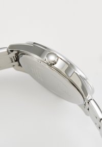 Montre en acier inoxydable avec un boîtier rond à surface polie, une couronne ronde proéminente et un bracelet métallique.