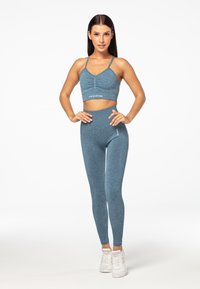 Plavi sportski set s crop topom sa trakama i detaljem na nabranju te visokim tajicama. Izrađeno od teksturirane, rastezljive tkanine.