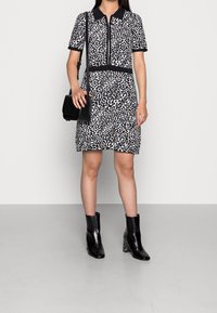 Robe imprimé léopard en noir et blanc avec un petit col, une fermeture éclair et une ceinture accentuée ; portée avec des bottines noires.