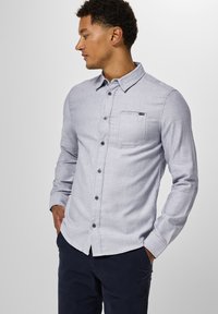 Camicia azzurro chiaro con maniche lunghe, taschino sul petto e un sottile motivo testurizzato. Rifinita con bottoni scuri.
