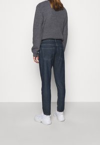 Vaqueros de mezclilla azul oscuro con un corte relajado, que cuentan con bolsillos traseros y una cinturilla plana, combinados con un suéter de punto gris y zapatillas blancas.