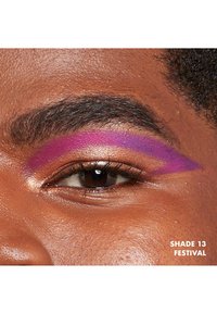 Ombretto audace in sfumatura viola sopra l'occhio, con un luccichio dorato sulla palpebra. Etichetta di testo: "SFUMATURA 13 FESTIVAL."