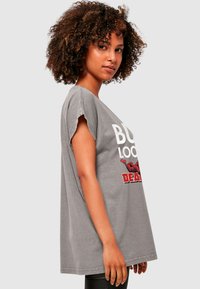 Šedé oversized tričko s krátkým rukávem. Na přední straně potisk bílým a červeným textem s grafickým designem. Měkká, ležérní tkanina.