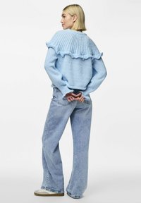 Svetlo modra pletena majica z volanastim dizajnom na ramenih, v kombinaciji s svetlo modrimi širokimi hlačami in belimi supergami.