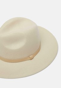 Cappello fedora in lana beige con una larga tesa e una fascia in pelle beige attorno alla base, caratterizzato da una texture liscia e un design minimalista.