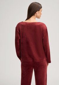 Burgunderfarbene Velour-Loungewear-Set, bestehend aus einem locker sitzenden Langarmoberteil mit weitem Ausschnitt und passenden Hosen mit weicher Textur.