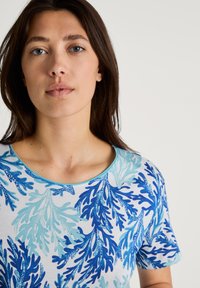 T-shirt a maniche corte in tessuto leggero con scollatura rotonda; il motivo presenta disegni di corallo blu e turchese su uno sfondo bianco.