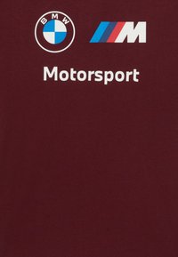 Tamsiai raudona medvilninė marškinė su BMW ir M logotipu balta ir mėlyna spalvomis, o žemiau atspausdintas tekstas "Motorsport".