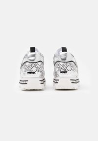 Scarpe athletic bianche con motivi geometrici neri, dettagli metallici argentati e suole bianche. Presentano una linguetta sul retro per una facile calzata.
