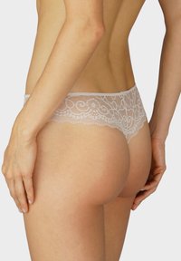 Culotte en dentelle beige clair, ornée de motifs floraux et de bords festonnés, avec une finition en tissu lisse et une taille extensible.
