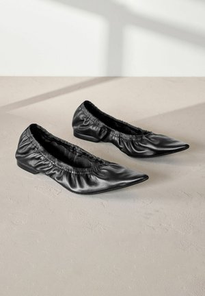 Fekete bőrbalerina lakások puha, ráncolt szélekkel és hegyes orral. Alacsony sarkú és sima textúrájú, kényelemre és könnyű viseletre tervezve.