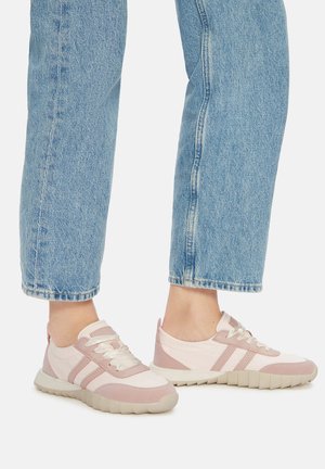 Zapatillas deportivas de color rosa claro y crema con tejido texturizado, cordones y suela de goma. Usadas con jeans azul denim de corte recto.