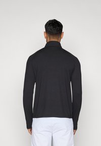 Polo cu mâneci lungi, de culoare neagră, cu guler, confecționat dintr-un material neted. Oferă o croială lejeră și un design simplu, fără modele sau accente suplimentare.