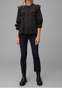 Black, ruffled blouse with a button-down front, long sleeves, and elastic cuffs, paired with dark jeans and chunky black boots.