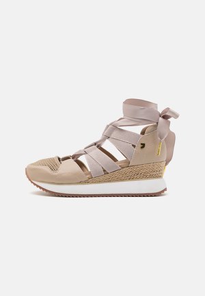 Baskets compensées beiges avec tige en mesh et cuir, dotées de brides élastiques croisées et d'une texture tissée au talon. Semelle blanche avec adhérence.