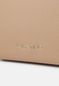 Beżowa torebka skórzana o teksturowej powierzchni z wygrawerowanym złotym logo "VALENTINO" na przodzie, charakteryzująca się prostymi liniami i minimalistycznym designem.